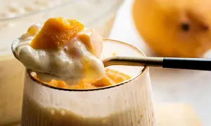 Słodkie monoporcje mango z kremowym deserem, podane w szklance. Obok leży dojrzałe mango.