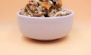 Tofu z pieczarkami w kremowym sosie, podane w białej miseczce.