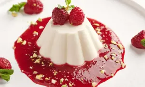 Delikatna tarta panna cotta z malinowym sosem, pistacjami i świeżymi malinami.