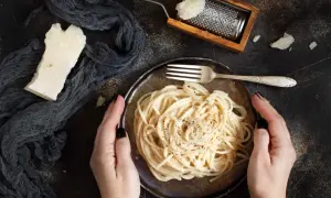 Idealny ser do spaghetti? Ten parmezan starty na tarce i kawałek obok talerza z makaronem sugerują odpowiedź.
