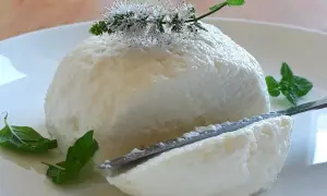 Puszysta, domowa ricotta na talerzu, ozdobiona kwiatami mięty. Nóż delikatnie kroi ser, odsłaniając jego kremową konsystencję.