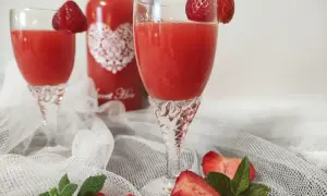 Idealny likier truskawkowy przepis. Dwa kieliszki z czerwonym napojem, ozdobione truskawkami, obok butelka i świeże owoce.