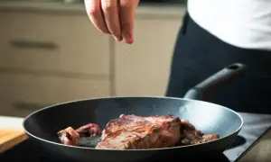 Ręka posypuje solą soczystego steka smażącego się na patelni.