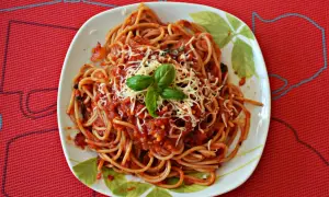 Pyszne spaghetti z pomidorami, posypane startym serem i udekorowane listkami bazylii. Idealne na szybki obiad.