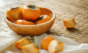 Koszyk pełen dojrzałych, pomarańczowych owoców kaki. Kilka pokrojonych kawałków leży obok, zachęcając do spróbowania, jak jeść kaki.