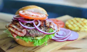 Pyszny, małomiasteczkowy burger z soczystą wołowiną, chrupiącym boczkiem, świeżą sałatą, pomidorem i czerwoną cebulą.
