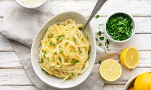 Pyszny makaron cytrynowy posypany parmezanem i świeżą natką pietruszki, obok połówki cytryny.