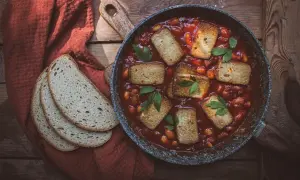 Aksamitne tofu w sosie pomidorowym z fasolką, podane w patelni, obok kromek chleba na rustykalnym stole.