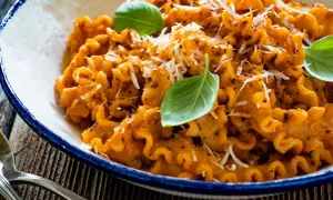 Pyszna włoska pasta z sosem pomidorowym, posypana parmezanem i udekorowana listkami bazylii. Idealna na obiad.