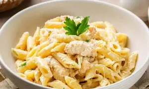 Pyszne danie z makaronem penne w kremowym sosie z kurczakiem, udekorowane natką pietruszki.