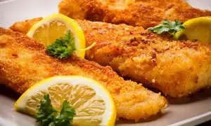 Chrupiące filety rybne w panierce panko, ozdobione plasterkami cytryny i natką pietruszki, kuszą apetycznym wyglądem.