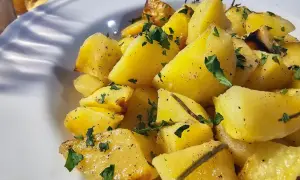 Pieczone ziemniaki pokrojone w ćwiartki, posypane natką pietruszki i pieprzem, podane na białym talerzu.