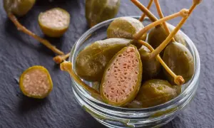 Zielone, marynowane kapary w szklanej miseczce. W przekroju widać ich charakterystyczną, ziarnistą strukturę. Zastanawiasz się, jak smakują kapary? Są lekko pikantne i orzeźwiające.
