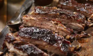 Soczyste żeberka w piwie, polane gęstym sosem BBQ, prezentują się apetycznie na drewnianej desce.