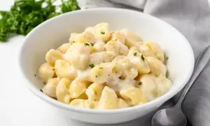 Miseczka kremowego mac and cheese, posypana natką pietruszki, obok łyżka i zielona gałązka.