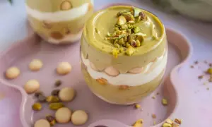 Pyszne tiramisu pistacjowe w szklance, przełożone kremem i biszkoptami, posypane posiekanymi pistacjami.
