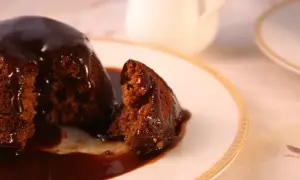 Pyszny, wilgotny deser sticky toffee, polany gęstym, karmelowym sosem, na eleganckim talerzyku.