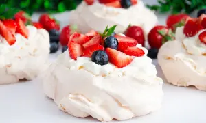 Mini bezy Pavlova z bitą śmietaną, truskawkami i borówkami. Delikatne, chrupiące na zewnątrz i miękkie w środku.