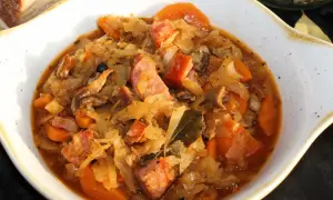 Bigos ze słodkiej kapusty Ani gotuje się powoli, by wydobyć głębię smaku. Widać kawałki kiełbasy, marchewki i liście laurowe.