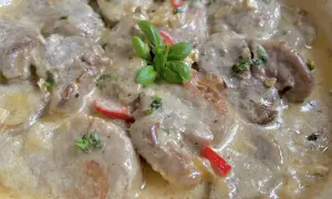 Soczyste polędwiczki w kremowym sosie camembert, udekorowane listkami bazylii i kawałkami papryki. Pyszne danie gotowe do podania.
