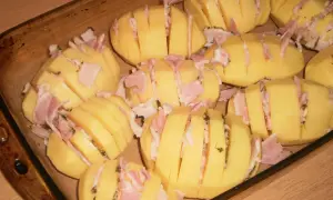 Ziemniaki hasselback z boczkiem i serem, gotowe do pieczenia w naczyniu żaroodpornym.