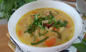 Aromatyczna zupa słodko kwaśna z kawałkami kiełbasy, ziemniaków i marchewki, udekorowana świeżymi ziołami.