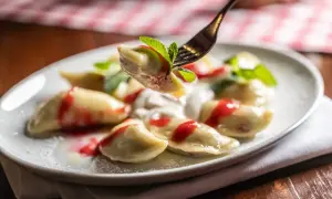 Jak gotować mrożone pierogi? Na talerzu pyszne pierogi z polewą truskawkową i miętą.