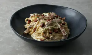 Pyszny przepis na carbonare: spaghetti z kremowym sosem, boczkiem i natką pietruszki w ciemnej misce.