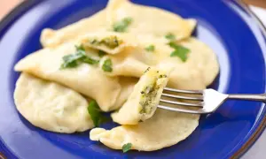 Pyszne pierogi ze szpinakiem i serem, udekorowane natką pietruszki, czekają na widelcu.