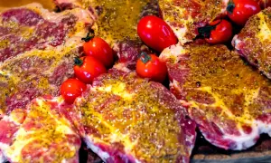 Karkówka wieprzowa, marynowana i przyprawiona, gotowa do grillowania, z pomidorkami koktajlowymi.