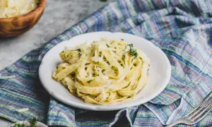 Pyszne fettuccine alfredo, bogato posypane parmezanem, na talerzu z kolorową serwetką.