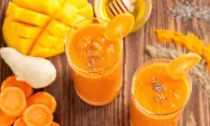 Dwa szklanki pomarańczowego koktajlu z mango i marchewki, ozdobione plasterkiem marchewki i nasionami chia.