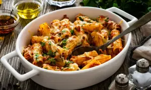 Pyszny obiad z mięsa mielonego: makaron rigatoni zapieczony z sosem bolońskim i ciągnącym serem, posypany świeżą natką pietruszki.