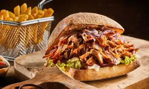 Apetyczny burger z szarpaną wieprzowiną, chrupiącymi frytkami i świeżą sałatą na drewnianej desce.