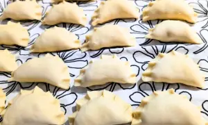 Rządki surowych, gotowych do gotowania, **weganskich pierogów** ułożonych na białym materiale z czarnymi, abstrakcyjnymi wzorami.