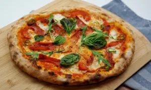 Pyszna pizza z rukolą, pomidorkami, papryczką i wędliną. Idealne dodatki do pizzy na drewnianej desce.