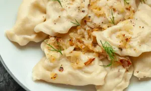 Pyszne pierogi z ziemniakami, okraszone cebulką i koperkiem, posypane pieprzem.