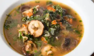 Aromaticzna, tradycyjna zupa grzybowa z kawałkami grzybów shiitake, zielonymi liśćmi i marchewką, podana w białej misce.