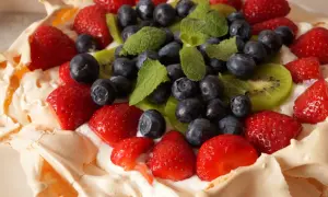 Pyszny tort bezowy z owocami: truskawki, borówki, kiwi i listki mięty na kremie.