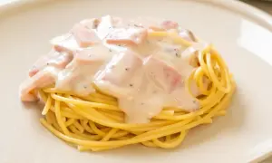 Pyszny makaron z pancettą i kremowym sosem, posypany pieprzem, na jasnym talerzu.