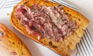 Chrupiąca grzanka z gęsią, doprawiona ziołami. Pyszna okrasa z gęsi na białym talerzu.