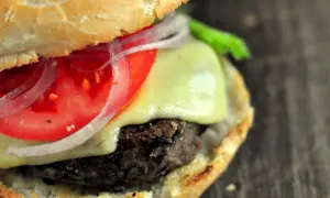 Pyszne burgery z czarnej fasoli z serem, pomidorem i czerwoną cebulą, podane w miękkiej bułce.