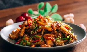 Chrupiąca wieprzowina po chińsku, z papryczkami chili i szczypiorkiem, na szarym talerzu.