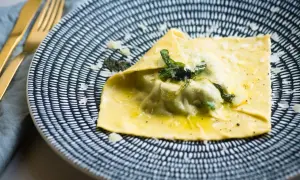 Duży raviolo con uovo, polany masłem i posypany parmezanem, na talerzu z czarno-białym wzorem.