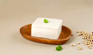 Kostka białego tofu na drewnianej desce, obok nasiona soi. Różne rodzaje tofu są wszechstronne w kuchni.