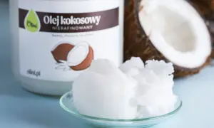Olej kokosowy nierafinowany na talerzyku, idealny jako jaki olej do smażenia. Obok połówka kokosa i słoik z etykietą.