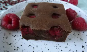 Pyszny fit brownie z fasoli, z malinami w środku i na talerzu. Idealny deser dla łasuchów.