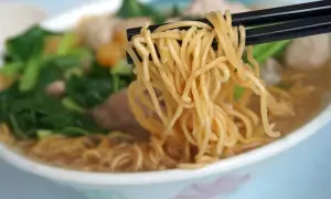 Chopsticks unoszą kłębek złocistego makaronu z miski pełnej aromatycznej domowej zupki chińskiej z warzywami i mięsem.