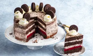 Pyszny tort oreo z kremem, malinową warstwą i ciasteczkami oreo na wierzchu. Kawałek ciasta na talerzyku.