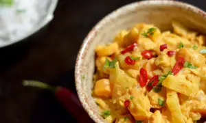 Pyszne danie z ziemniaków i warzyw w kremowym sosie co z mleczka kokosowego, ozdobione papryczką chili i natką pietruszki.